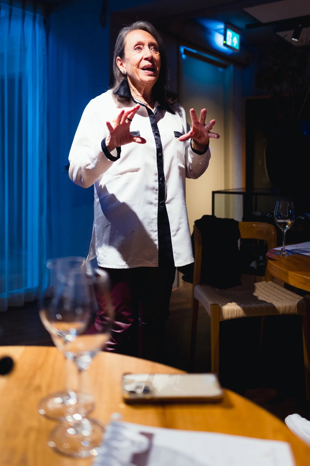 Marimar Torres speaking and gesturing with both hands while addressing diners at a table