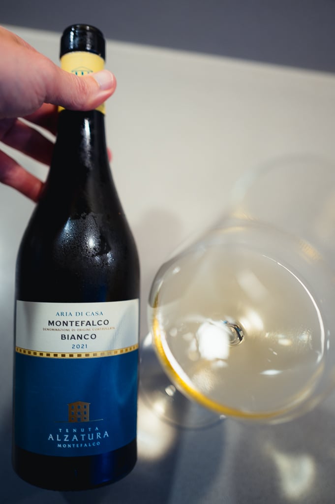 Hand holding the Aria di Casa Montefalco Bianco bottle next to a tilted glass of white wine
