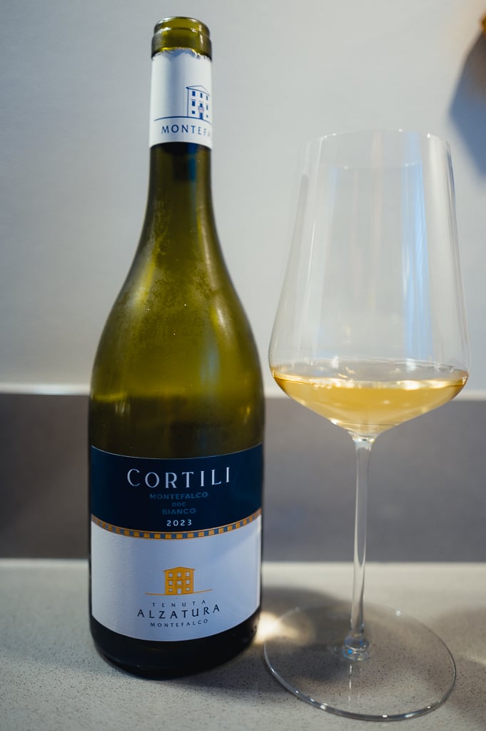 Cortili Montefalco Bianco 2023 bottle next to a glass of pale golden white wine