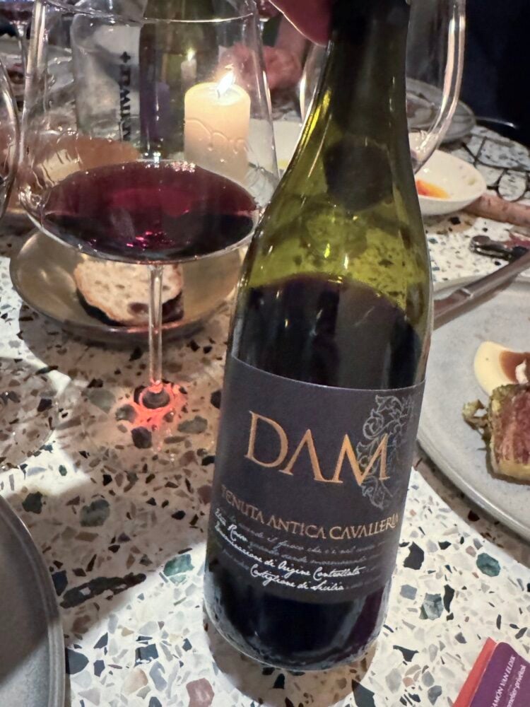Dark Dame red wine bottle from Tenuta Antica Cavalleria with a glass of red wine on a terrazzo table