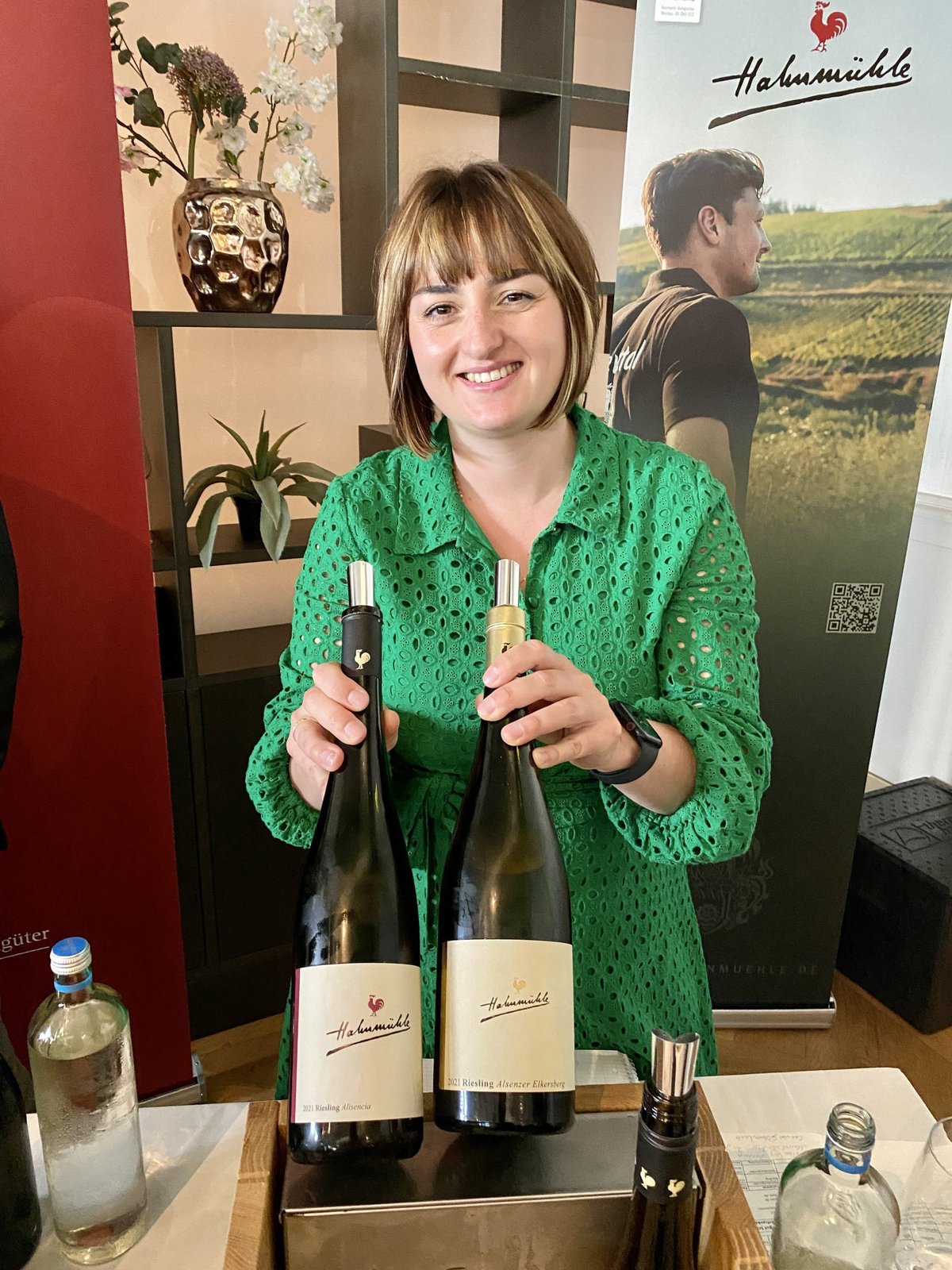 Woman in a green dress at the Hahnmühle stand holding two Riesling bottles