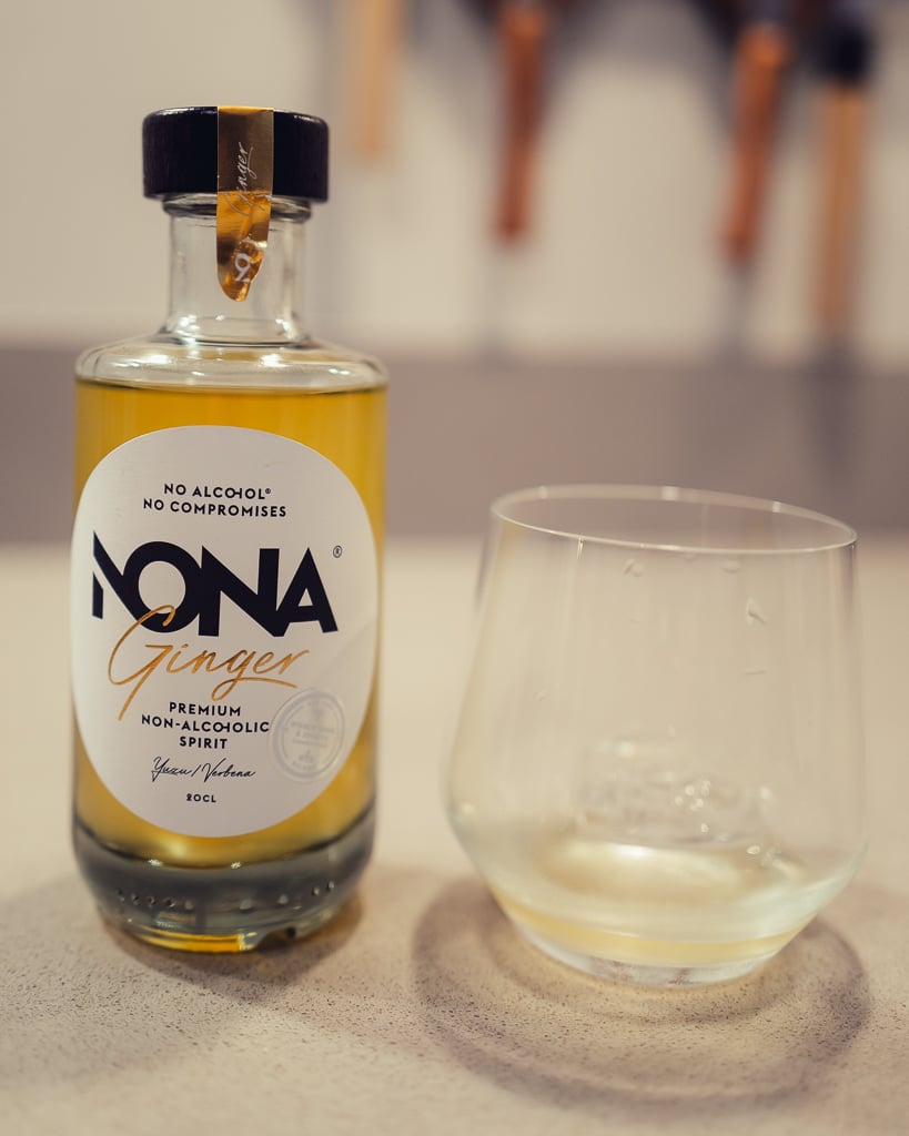 NONA Ginger non-alcoholic spirit bottle with yellow liquid beside an empty tumbler