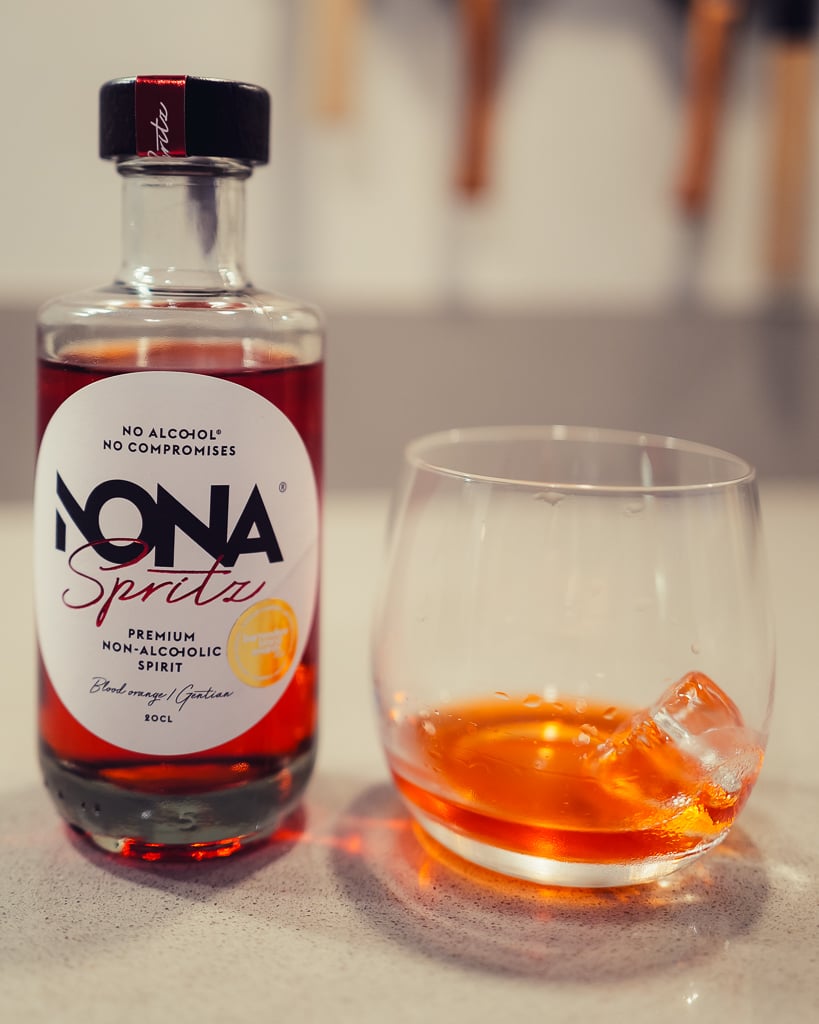 NONA Spritz non-alcoholic spirit bottle beside a glass of amber drink over ice