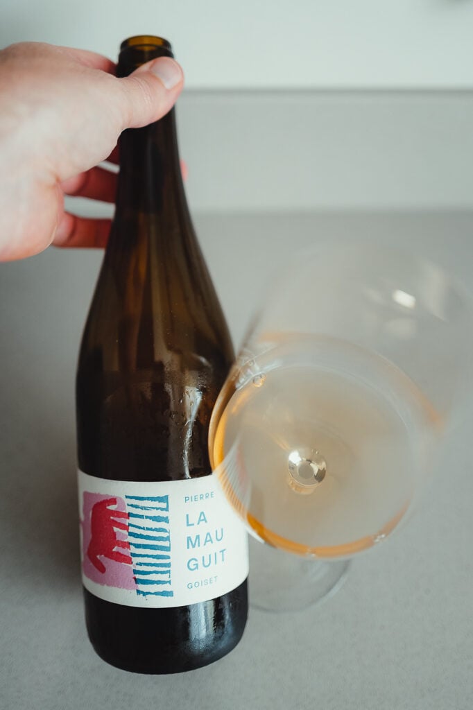 Hand holding the Pierre Goiset La Mauguit bottle next to a tilted glass of orange wine