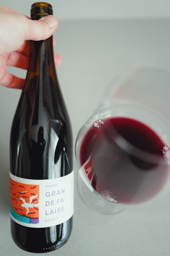 Hand holding the Pierre Goiset Gran de Falaise red wine bottle next to a glass of red