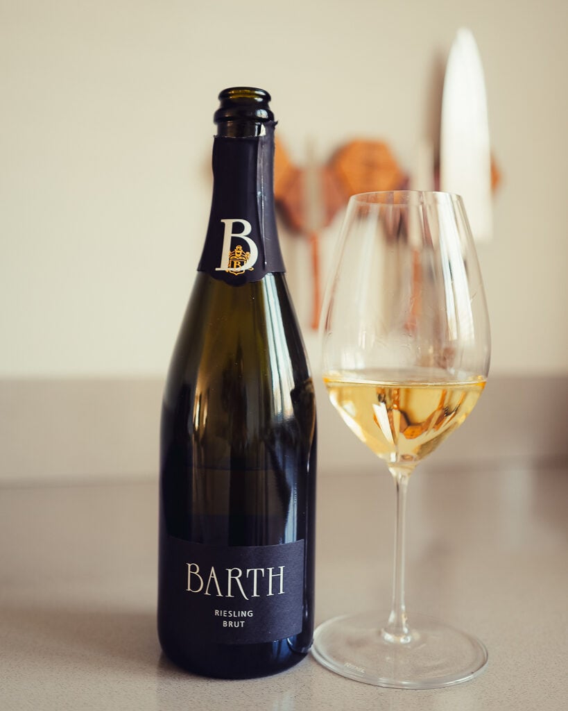Dark bottle of Barth Riesling Brut beside a glass of golden sparkling wine