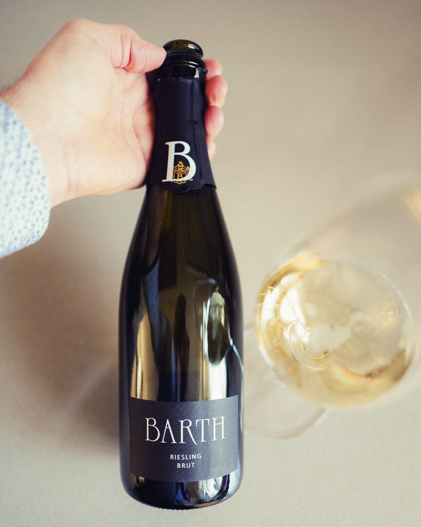 Hand holding the Barth Riesling Brut bottle by the neck next to a glass