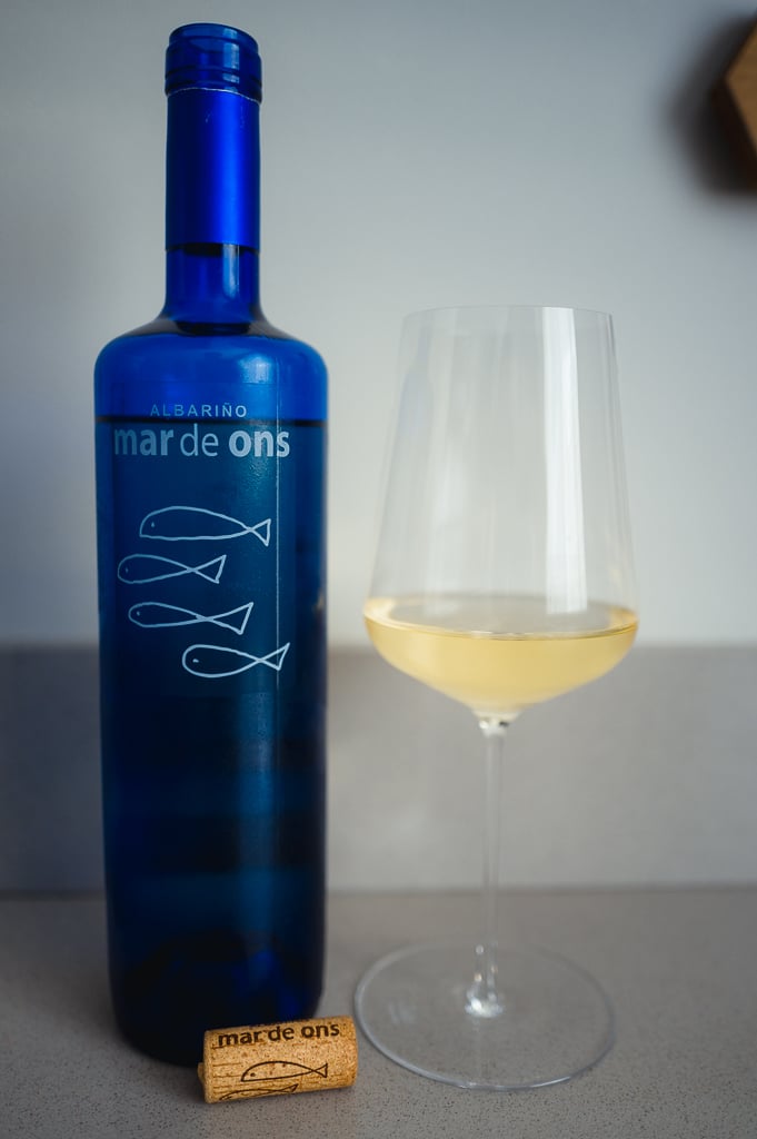 Blue Mar de Ons bottle, a glass of white wine and the fish-marked cork on a counter