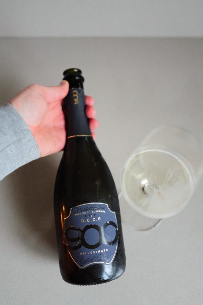 Hand holding the dark 900 Valdobbiadene DOCG bottle beside a glass of sparkling wine