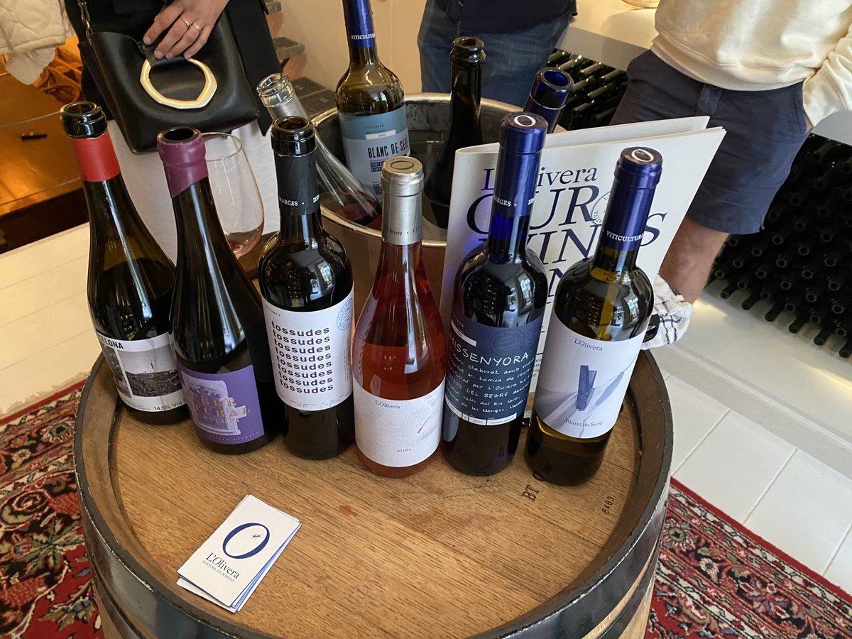 Lineup of L'Olivera and Can Calopa wine bottles arranged on a wooden barrel