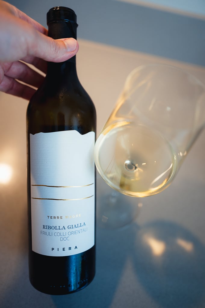 Hand holding the Piera Terre Magre Ribolla Gialla bottle beside a glass of white wine