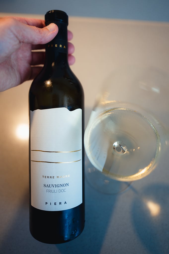Hand holding the Piera Terre Magre Sauvignon bottle next to a glass of white wine
