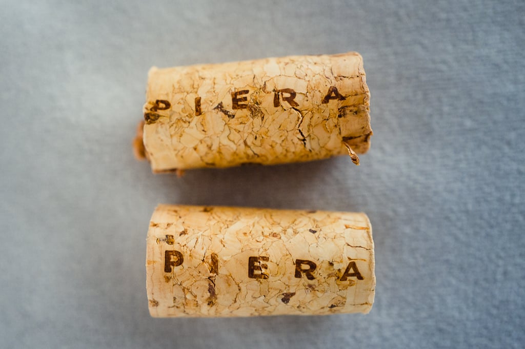 Two natural corks branded PIERA lying on a grey surface