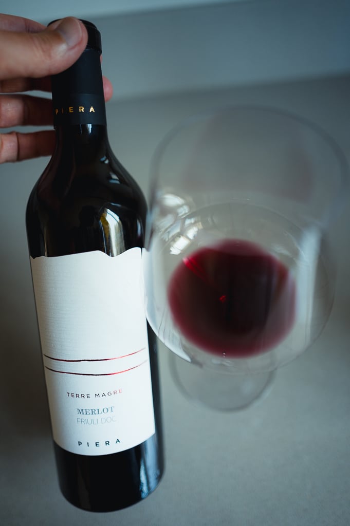 Hand holding the Piera Terre Magre Merlot bottle beside a glass of red wine