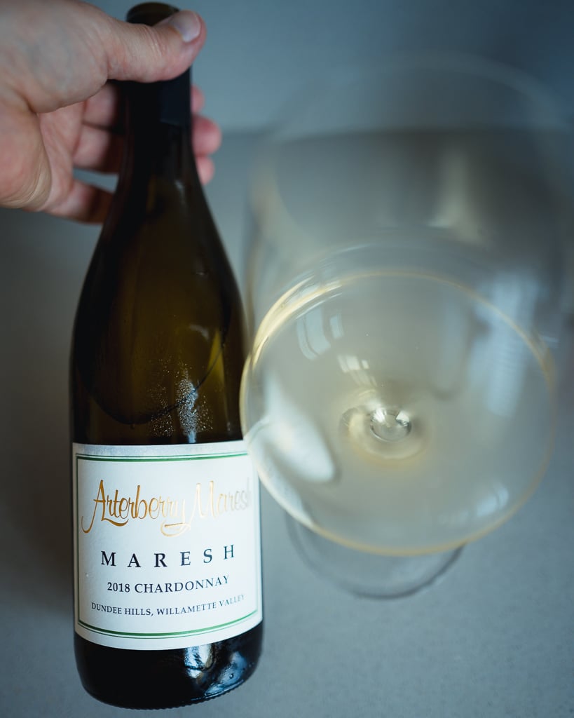 Hand houdt fles Arterberry Maresh Maresh 2018 Chardonnay naast een glas witte wijn