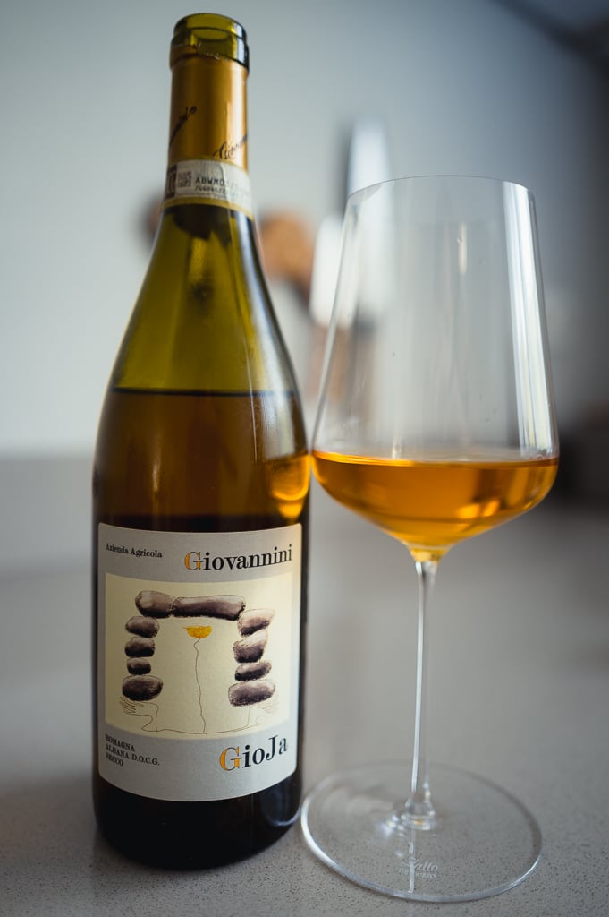 Giovannini Albana bottle lying angled next to a glass of amber-orange wine