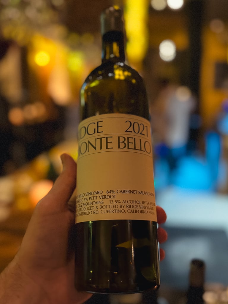 Hand holding the Ridge Monte Bello 2021 bottle in the warmly lit wine bar
