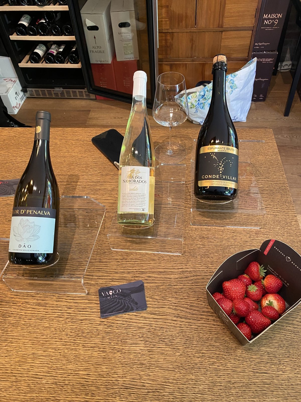 Three Portuguese wines and a Vasco card on a table with a box of strawberries