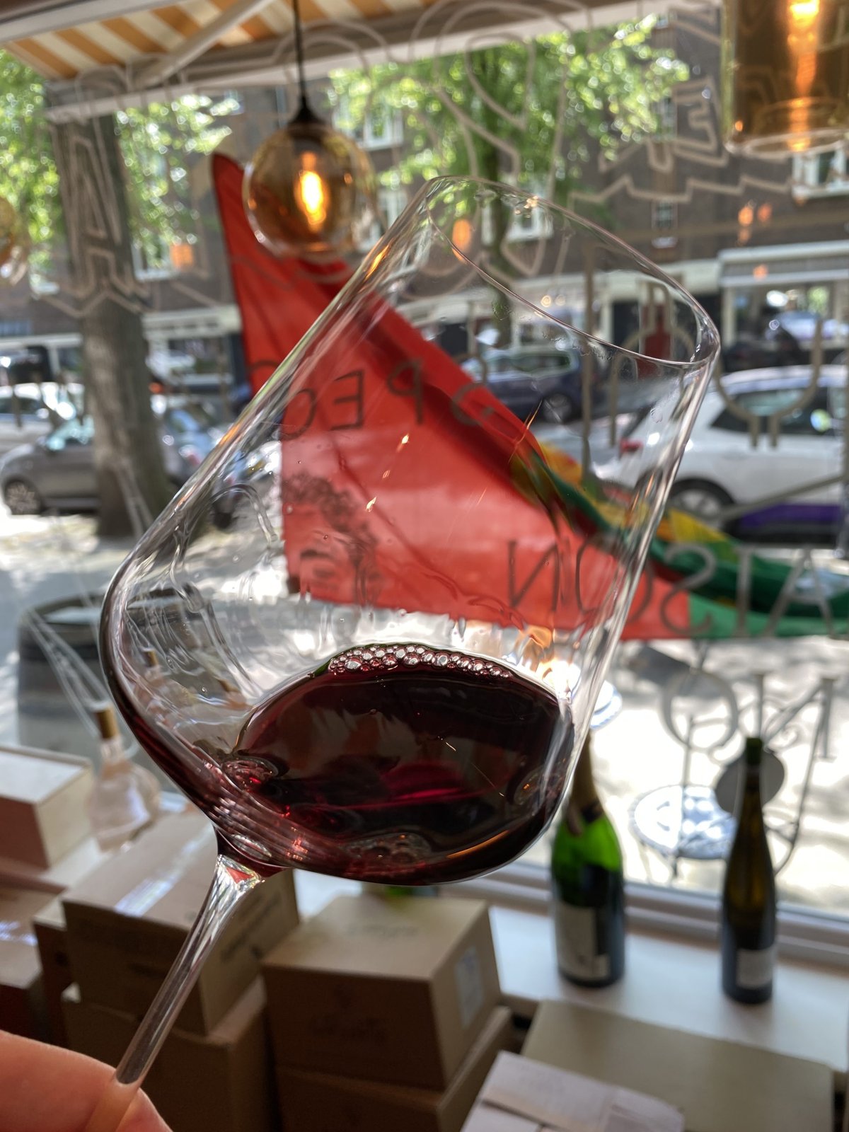 Glass of red wine held up by a shop window looking out on an Amsterdam street