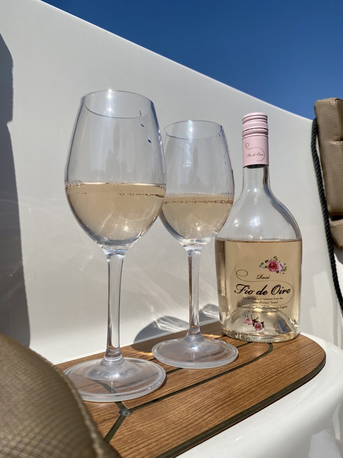 Two glasses of pale rosé and a Fio de Oiro bottle on a boat table under blue sky