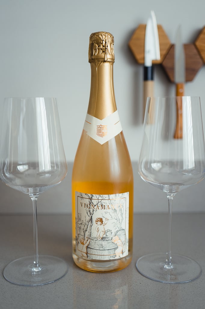 Salmon-pink Vignamante sparkling bottle with cherub label, flanked by two empty wine glasses on a kitchen counter
