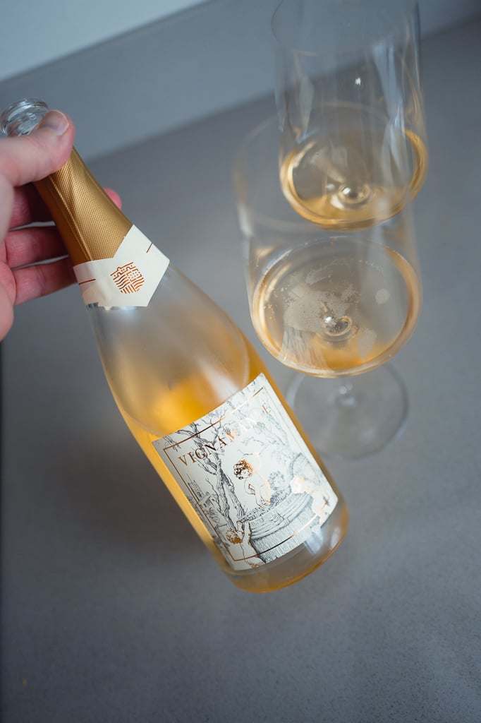 Hand tilting the Vignamante bottle beside two glasses of salmon-coloured sparkling wine