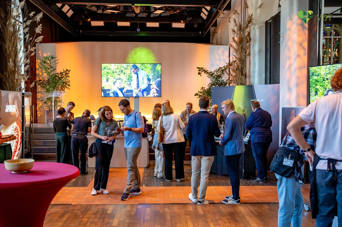 Tasting hall with a video screen and producer stands, guests standing at high tables sampling champagne on a wooden floor