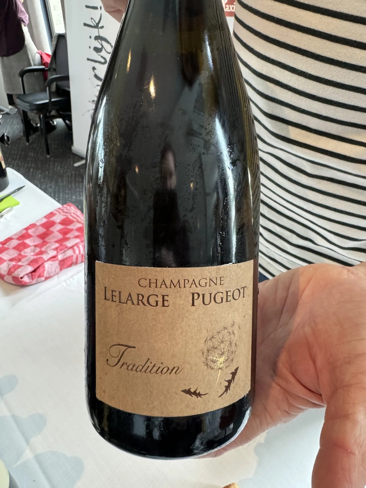 Champagne Lelarge-Pugeot Tradition bottle with a kraft-brown label and a dandelion motif, held in one hand