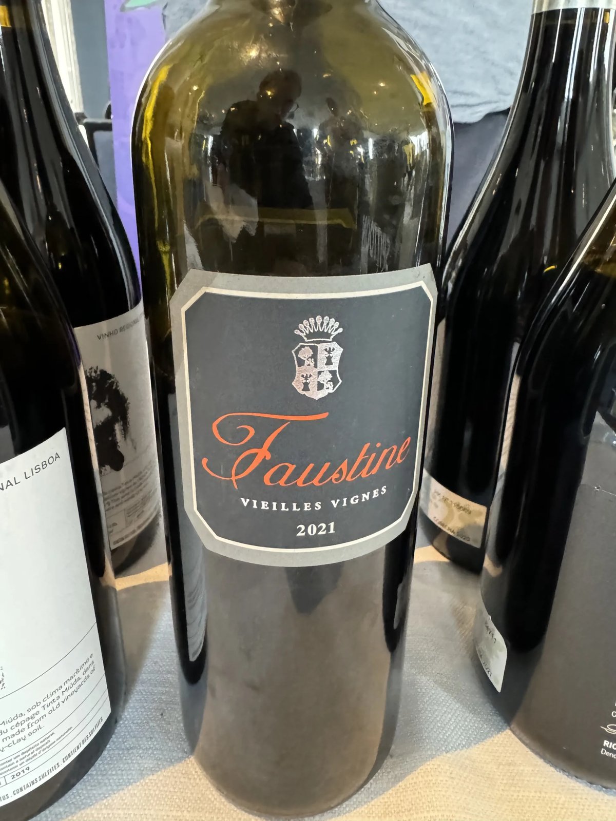 Bottle with a black Faustine Vieilles Vignes 2021 label and orange script, flanked by other red wines