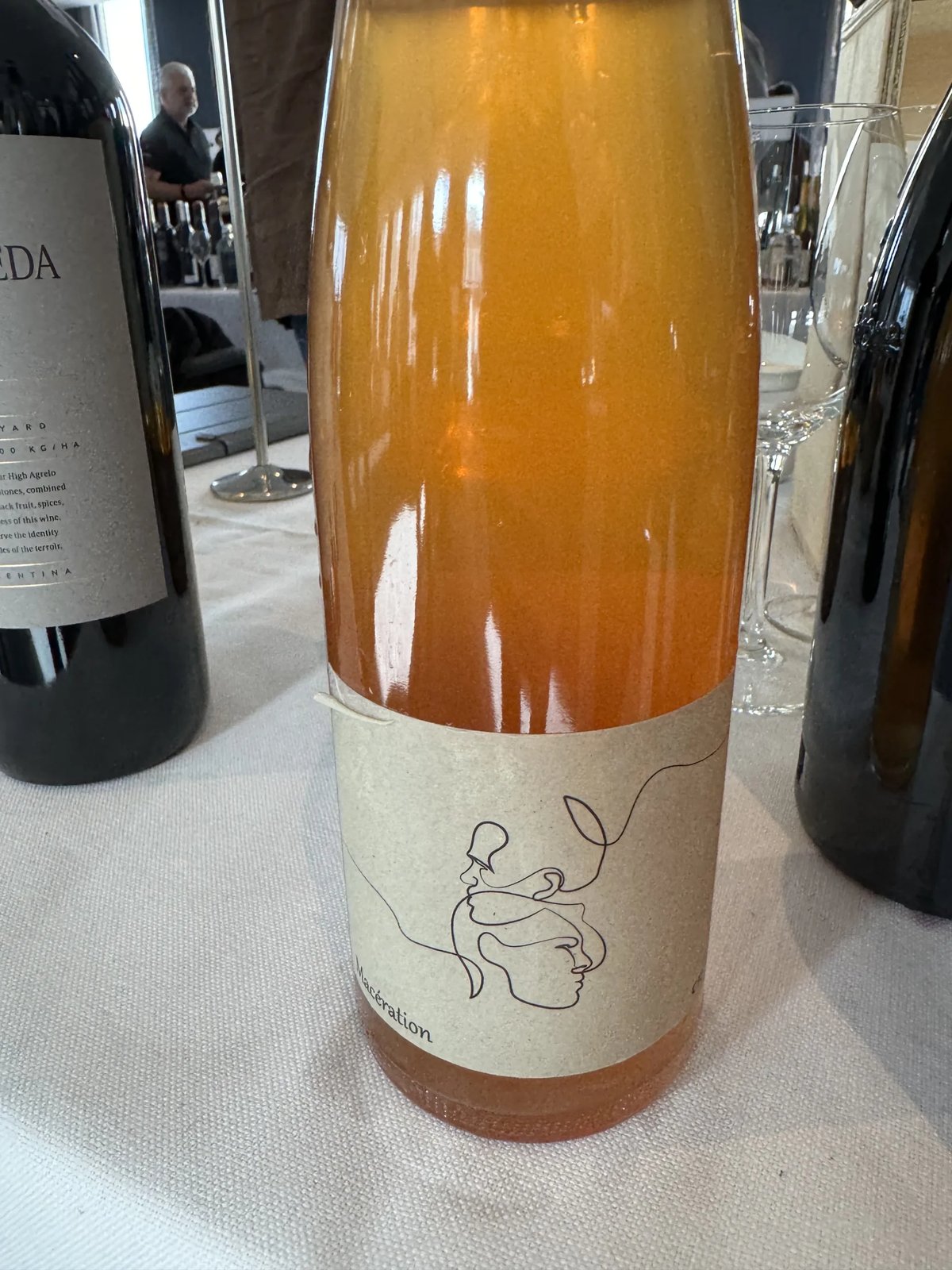 Orange-hued wine bottle with a pale label showing a single-line drawing of a face, on a tasting table