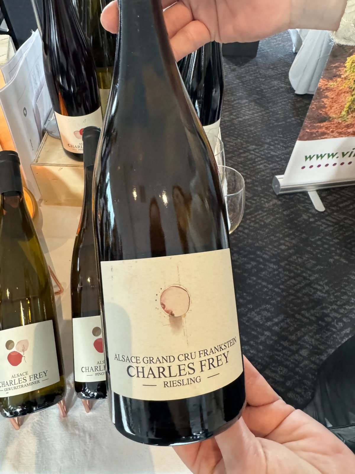 Hand holding a Charles Frey Riesling Alsace Grand Cru Frankstein bottle, with other Charles Frey bottles behind