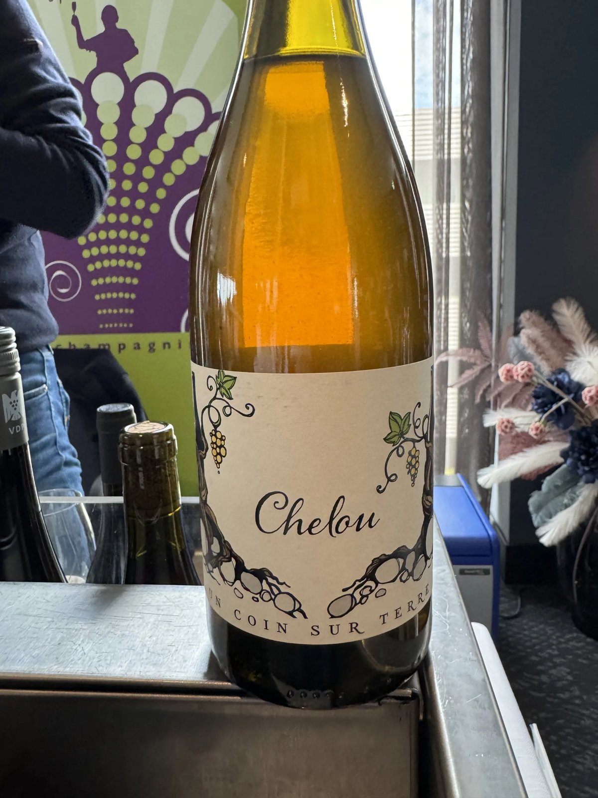 Amber-coloured Chelou bottle with a vine-drawn label reading Un coin sur terre, on a metal tasting counter