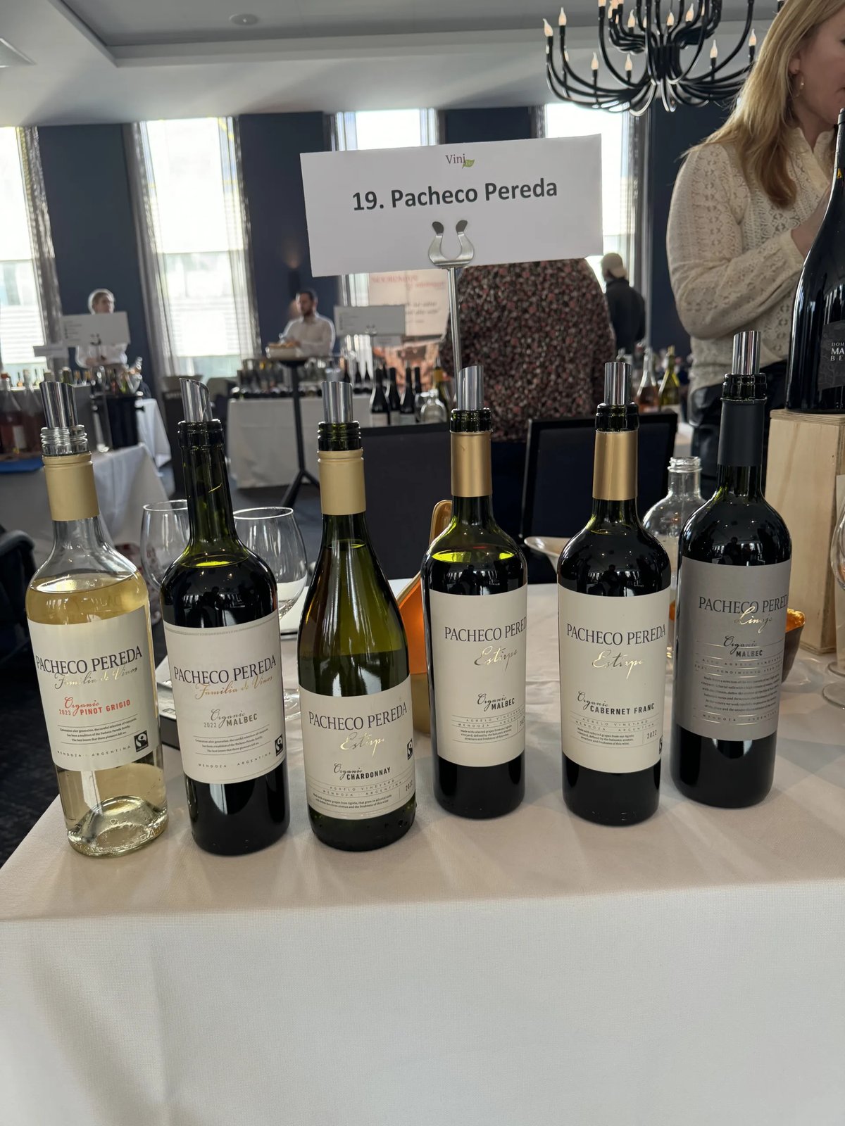 Row of six Pacheco Pereda bottles on a white-clothed table beneath a printed sign reading 19. Pacheco Pereda