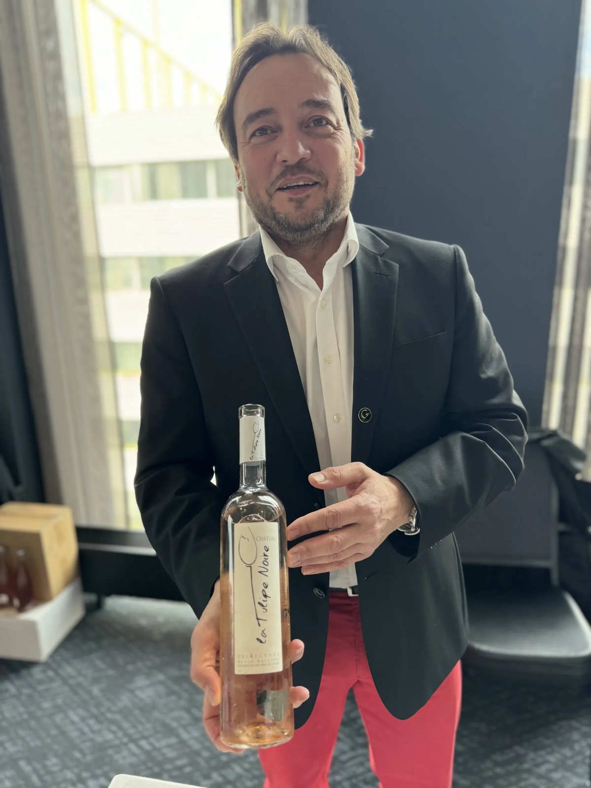 Man in a dark blazer and pink trousers holding a Château La Tulipe Noire rosé bottle at the tasting