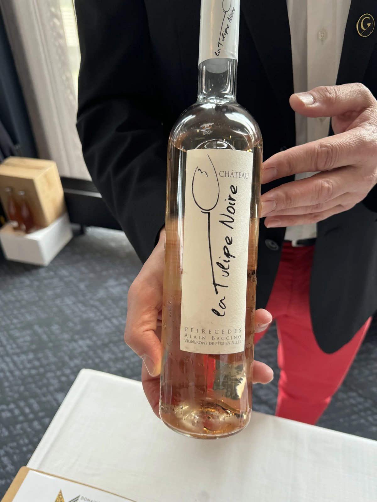 Pale rosé Château La Tulipe Noire bottle held up close, with a black tulip drawn on the cream label