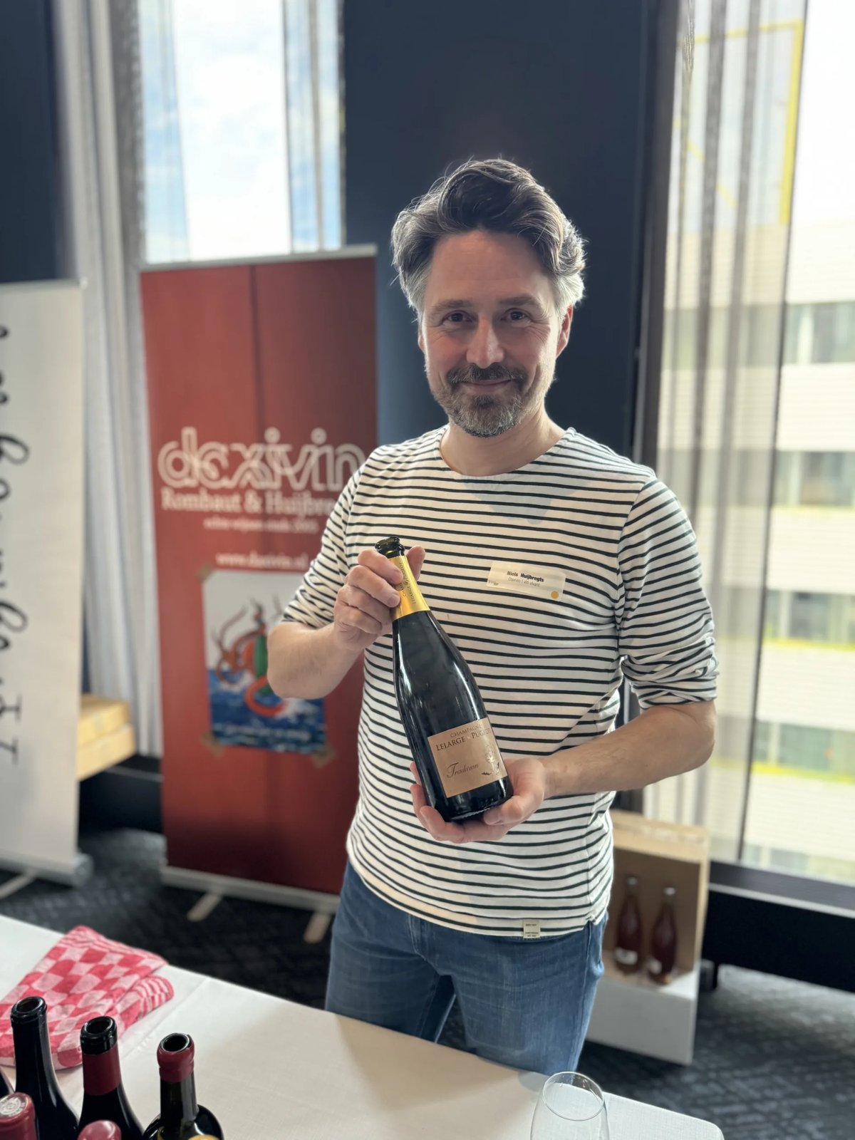 Man in a striped shirt at the Daxivin stand holding a champagne bottle by the neck