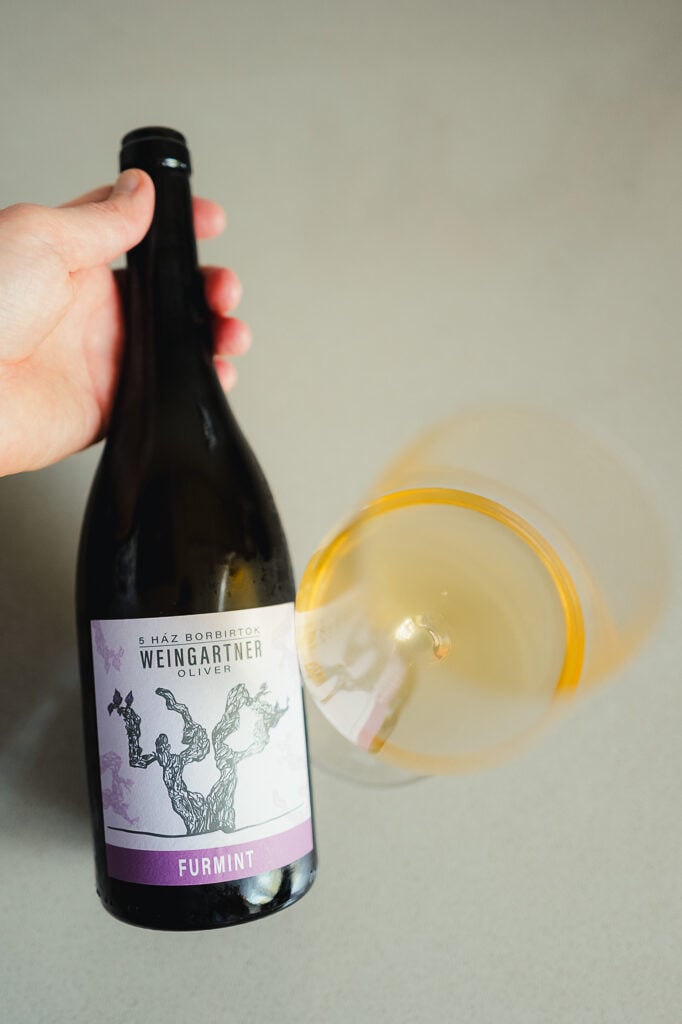 Hand holding the Weingartner Furmint bottle while pouring pale wine into a tilted glass