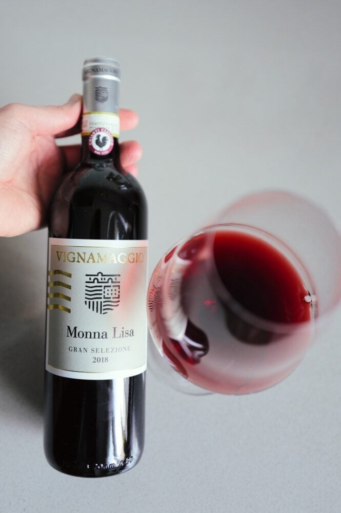 Hand holding the Vignamaggio Monna Lisa 2018 bottle beside a tilted glass of red wine