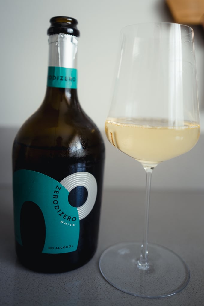 ZeroDiZero White bottle with a teal label beside a stemmed glass of pale golden sparkling drink