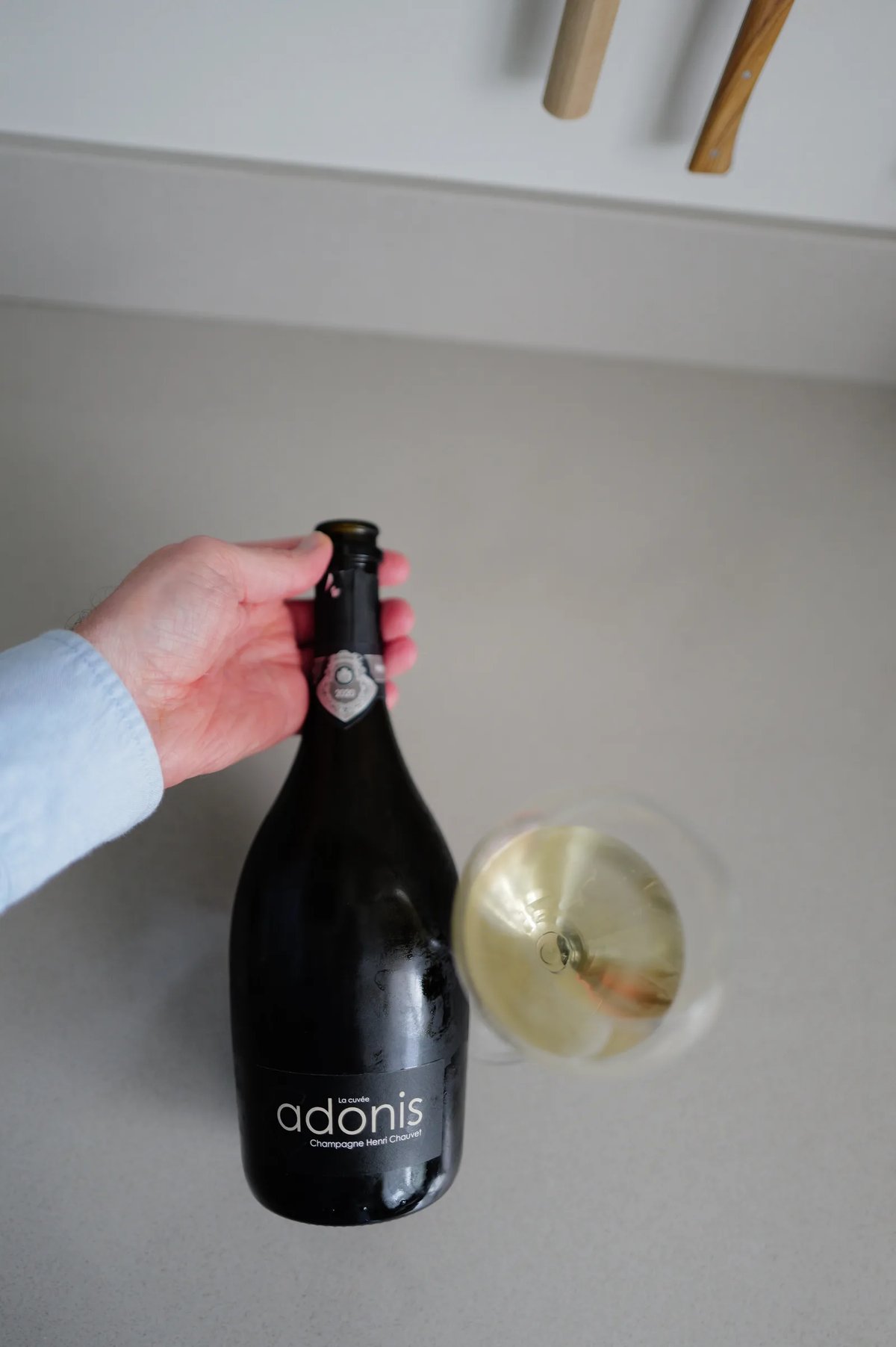 Bottle of Henri Chauvet Adonis 2020 showing the front label, next to a glass of champagne