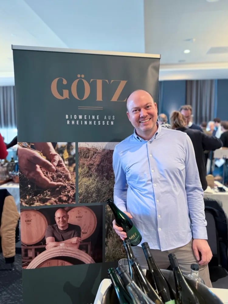 Holger Götz portrait holding a bottle in front of the Weingut Götz banner