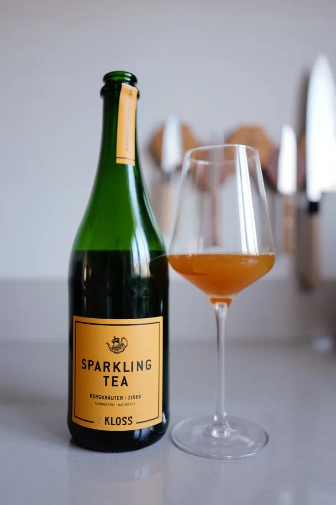 Bottle of C. Kloss Sparkling Tea Bergkraeuter with a yellow label, next to a glass of orange tea