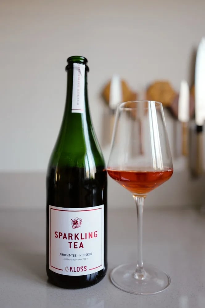 Bottle of C. Kloss Sparkling Tea Fruit Tea with a white and red label, next to a glass of red-orange tea