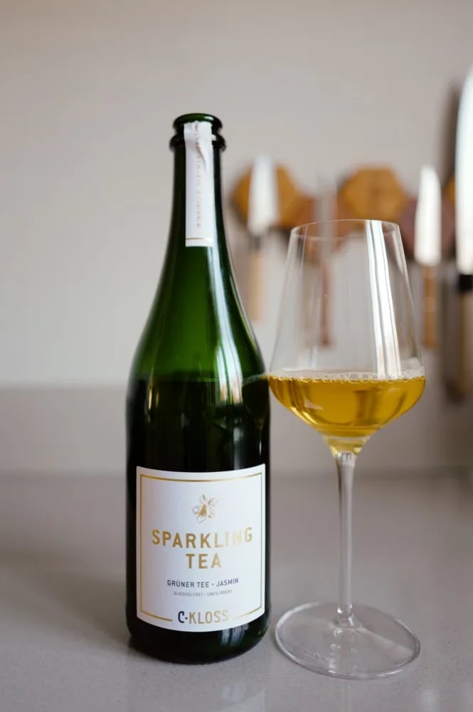 Bottle of C. Kloss Sparkling Tea Green Tea with a white label, next to a glass of golden tea
