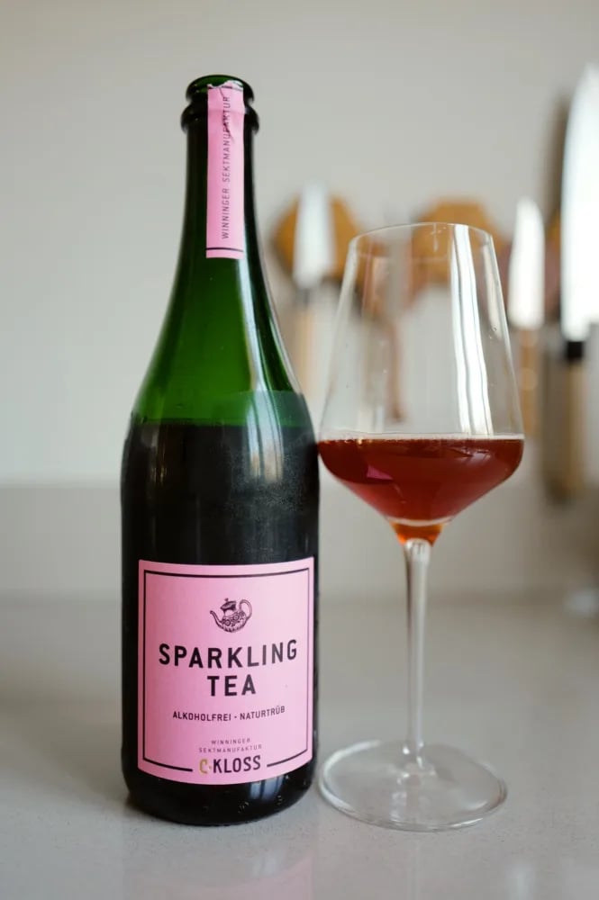 Bottle of C. Kloss Sparkling Tea Rose with a pink label, next to a glass of red tea