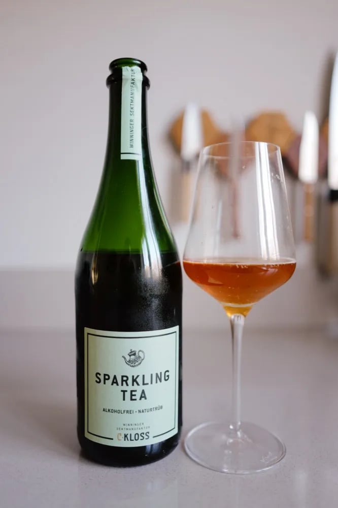 Bottle of C. Kloss Sparkling Tea Weiss with a mint green label, next to a glass of amber tea