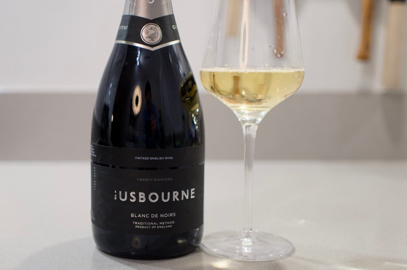 Gusbourne Blanc de Noirs 2018 bottle and glass with English vineyard