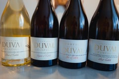 Four bottles of Champagne Edouard Duval lined up on a wooden table, with the Côte des Bar vineyard hillside in the background.
