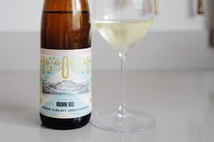 Bottle of Kolonne Null Gelblack alcohol-free Riesling next to a glass of white wine on a light kitchen counter