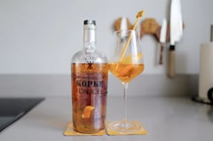 Bottle of Kopke On Ice white port next to a wine glass with three ice cubes and a twist of orange peel on a kitchen counter